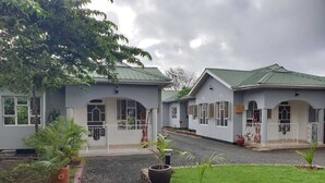 A building with a green roof and white walls, featuring a paved entrance and potted plants. - Le Parlour (Boma la Ngombe)