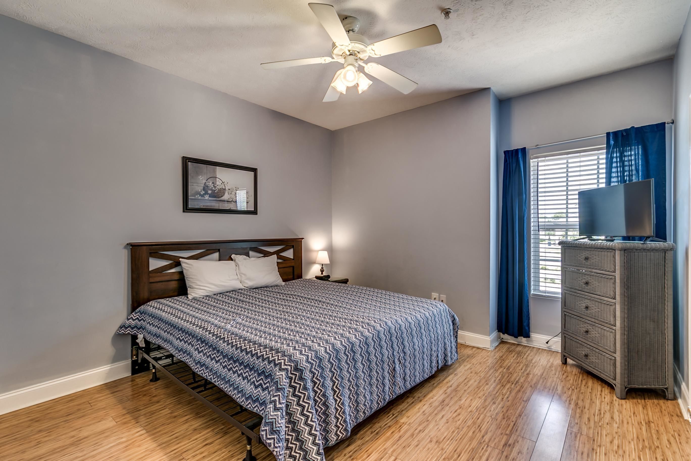 A bedroom with a bed, a ceiling fan, a dresser, and a window with curtains.