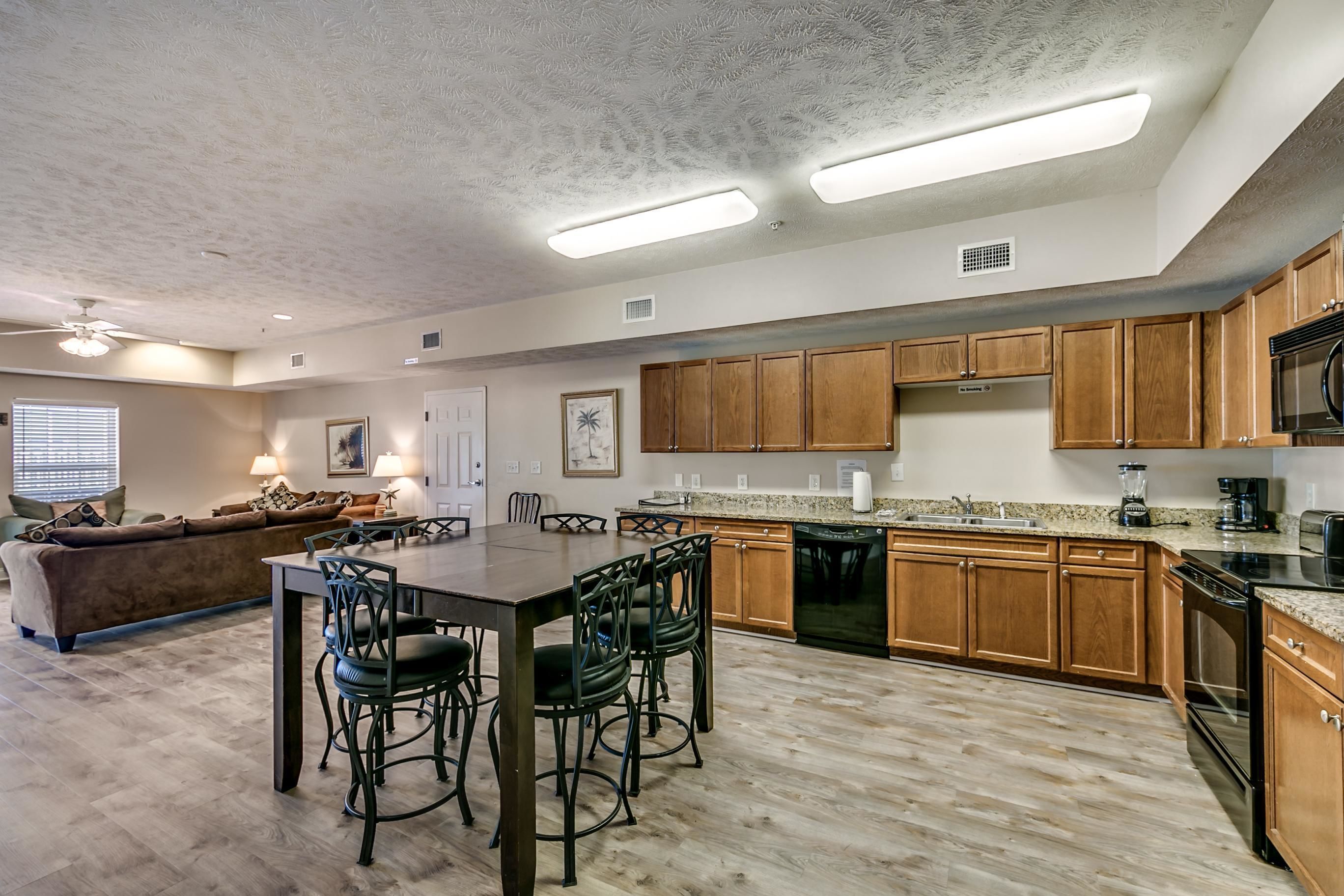 A spacious kitchen with wooden cabinets, a dining area with chairs, and a living room with a sofa and lamps.