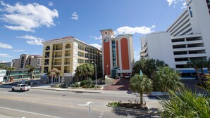 A hotel with a prominent clock tower, a parking garage, and a street view with palm trees. - Myrtle Beach 201B Villa Villa 4 (Myrtle Beach)