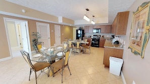 A spacious kitchen with modern appliances, a dining area with glass tables and chairs, and a large wooden cabinet.