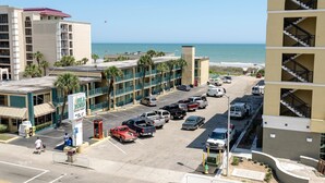 A hotel with a parking lot, a beach view, and a building with a red roof.