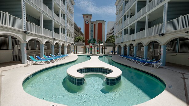 A hotel pool area with a 3 FT depth marker, lounge chairs, and a central water feature.