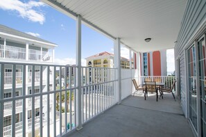 A covered balcony with a table and chairs, overlooking a street with buildings.