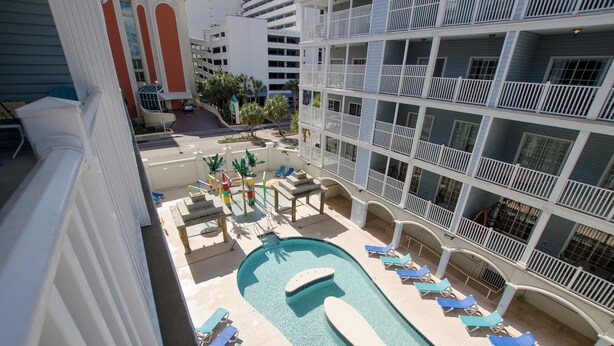 Zona de piscina con sillones de descanso y una piscina pequeña, rodeada por un edificio de varios pisos con balcones.