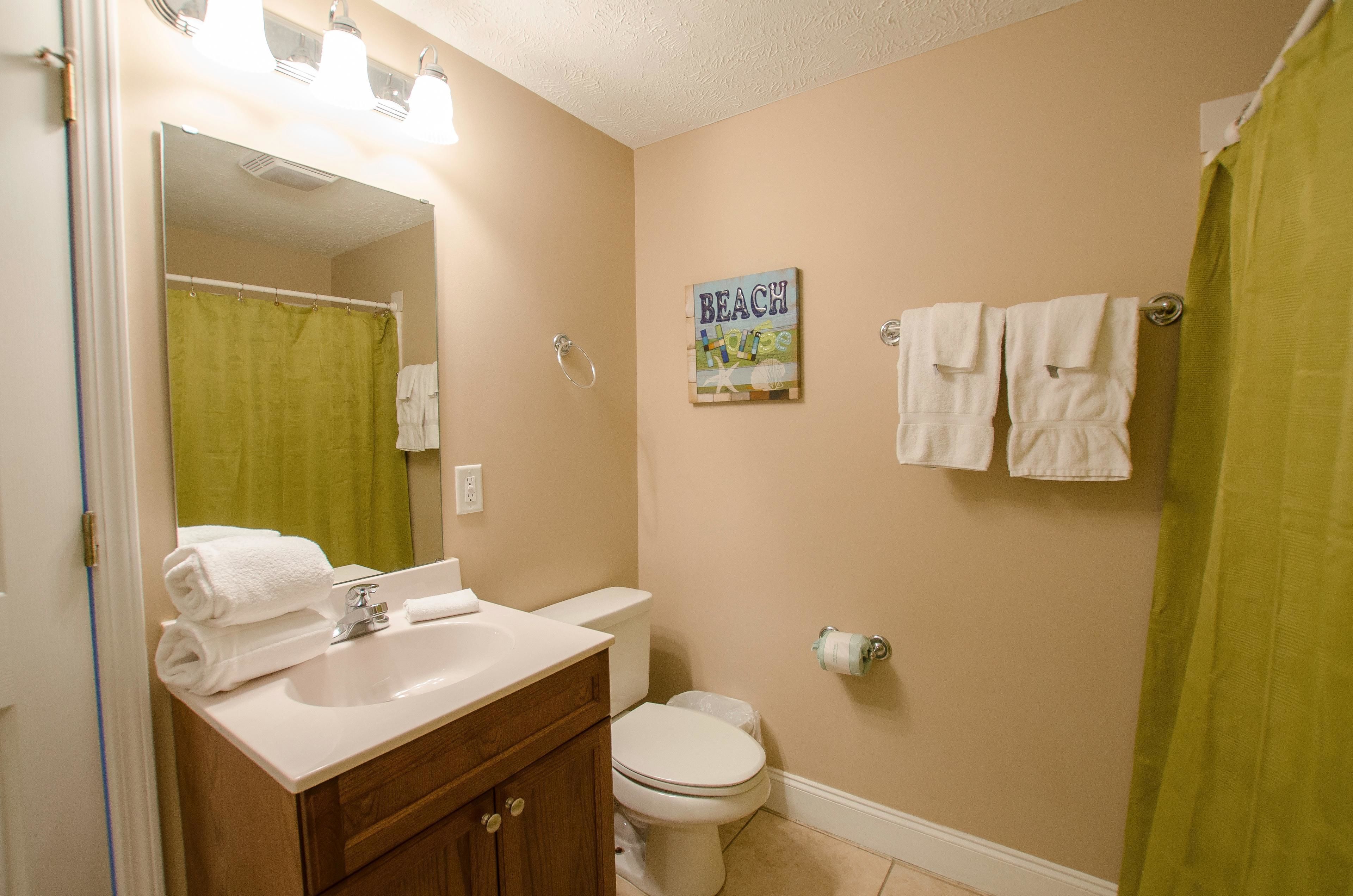 Een badkamer met een wastafel, spiegel, toilet en een groene douchegordijn.
