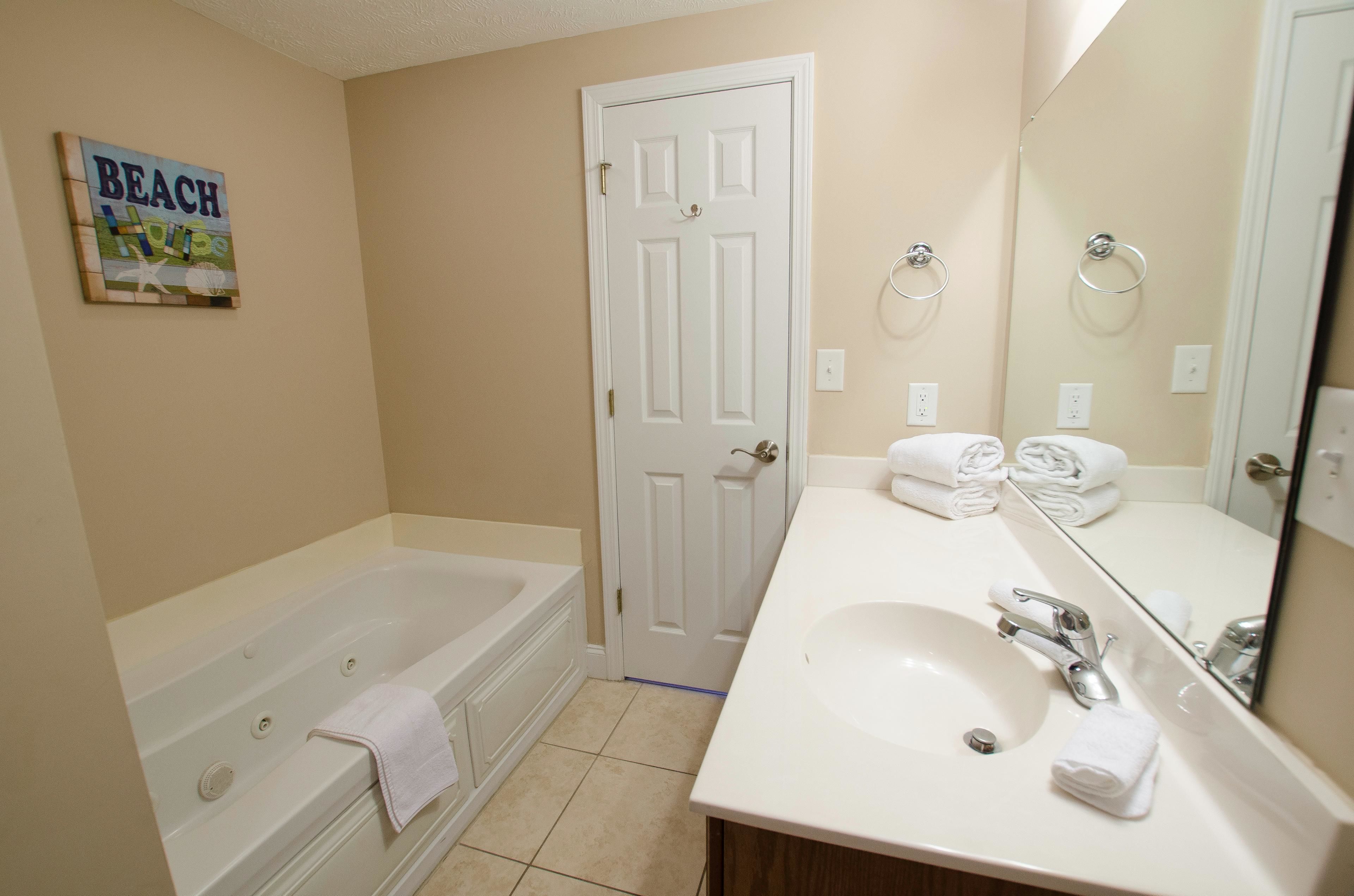 A bathroom with a bathtub, a sink, a mirror, and a door.