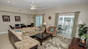 A living room with a sectional sofa, a coffee table, and a dining area with chairs. There is a balcony with a railing and a view of the outside. - Myrtle Beach 303B Villa Villa 6 (Myrtle Beach)
