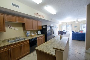 Enjoy cooking in this well-equipped kitchen with a refrigerator, dishwasher, and sink, connected to a dining area with a comfortable couch and natural light.
