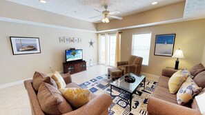 A living room with beige walls, a ceiling fan, a flat-screen TV, wicker furniture, a patterned rug, and framed pictures on the wall. - Myrtle Beach 305A Villa Villa 4 (Myrtle Beach)