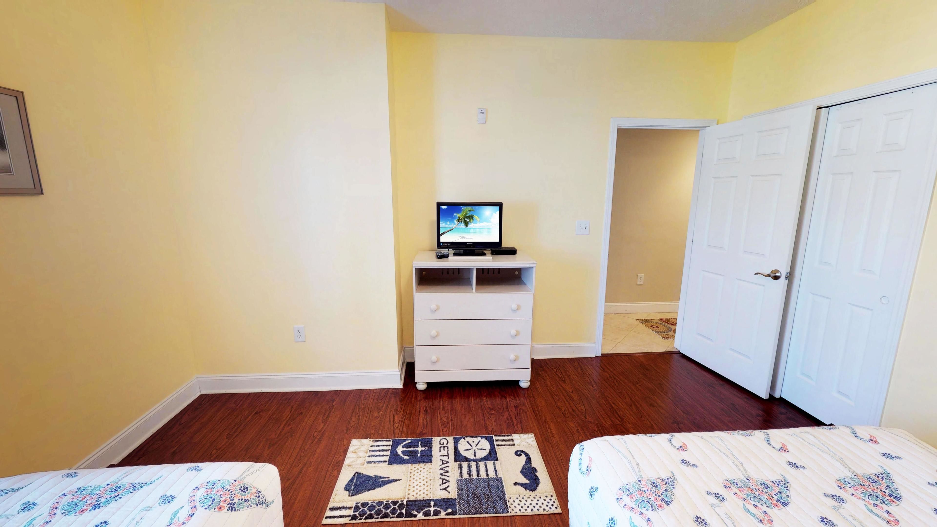 A room with a bed, a TV on a stand, a wardrobe, and a patterned rug.