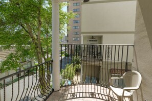 Een balkon met een witte stoel, een tafeltje en uitzicht op een gebouw en bomen.