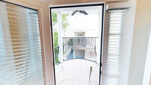 A view through a door into a balcony area with a tiled floor, a metal railing, and a hanging ceiling fan.