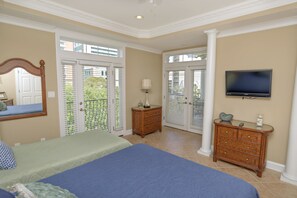 Een slaapkamer met een groot bed, een kast, een televisie en een openslaande deur naar een balkon.