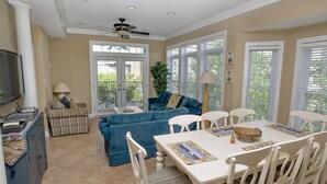 A spacious living area with a blue sofa, a dining table with chairs, and a ceiling fan.
