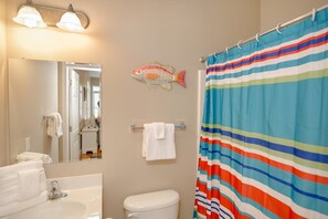 A bathroom with a striped shower curtain, a white sink, a toilet, a mirror, and a fish decoration on the wall. - Tuscan Ocean Vista B Holiday Home Holiday home 8 (Myrtle Beach)