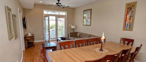 A dining area with a wooden table and chairs, a ceiling fan, and a view of the outside through a glass door.