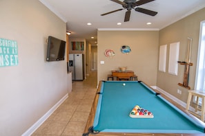 Una mesa de billar con bola blanca y bolas de pool, un ventilador de techo y un televisor en la pared.