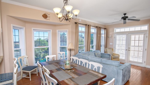A spacious dining area with a wooden table and white chairs, a blue sofa, and a chandelier. - Tuscan Ocean Vista D Holiday Home Holiday home 8 (Myrtle Beach)