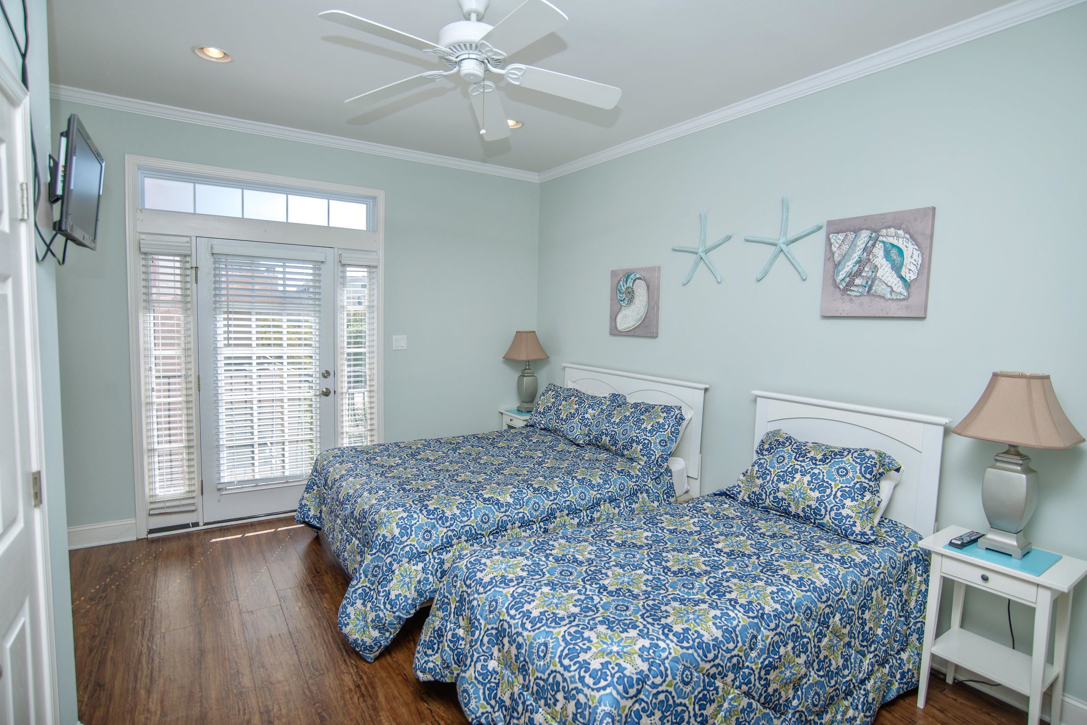 A bedroom with two beds, a ceiling fan, a nightstand with a lamp, and artwork on the wall.