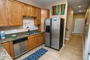 Una cocina con armarios de madera, un refrigerador de acero inoxidable, lavavajillas y encimera de granito.