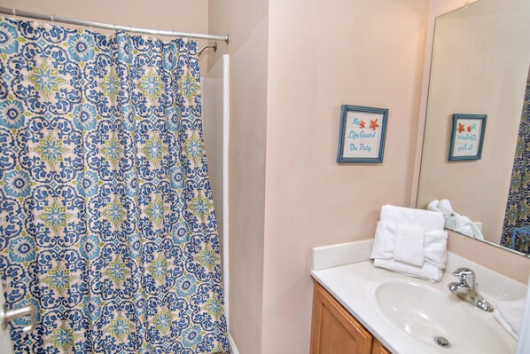 A bathroom with a patterned shower curtain, a sink, and two framed motivational quotes on the wall.