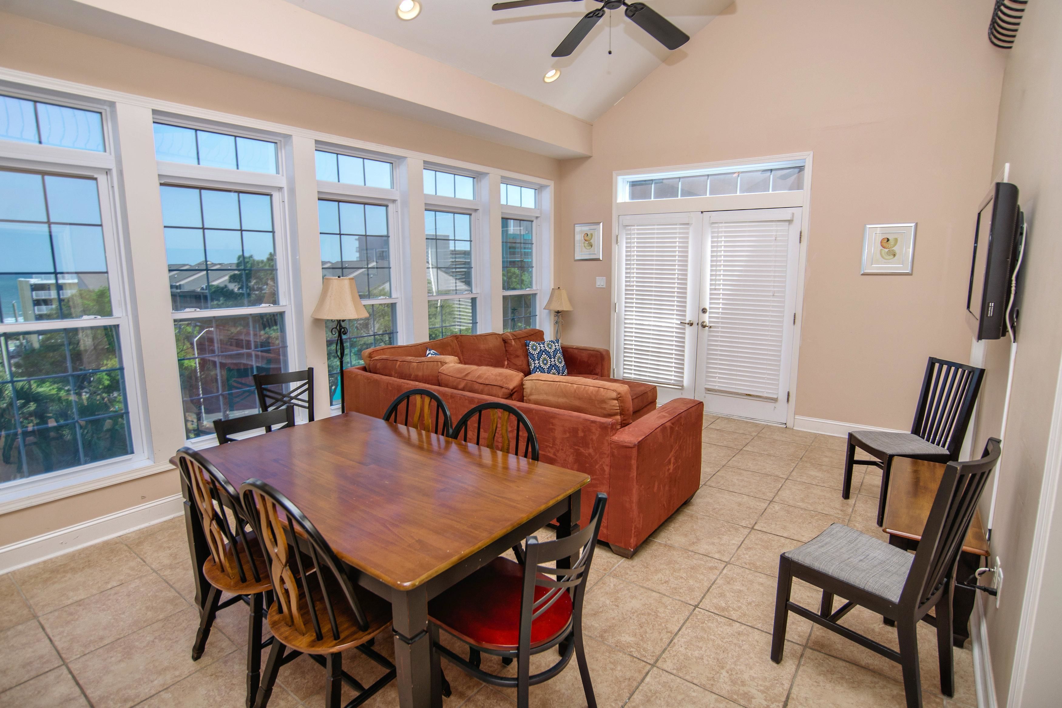 A spacious living room with a wooden dining table and chairs, a brown sofa, and a ceiling fan.