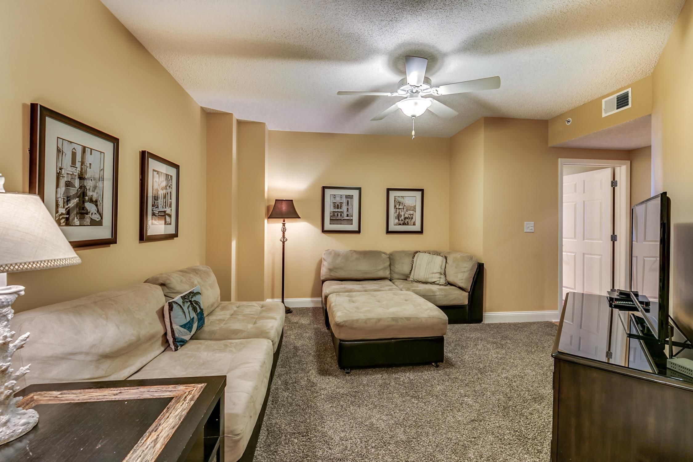 A living room with a beige sofa, a coffee table, a floor lamp, and a ceiling fan.