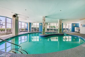An indoor swimming pool with clear blue water, surrounded by large windows and a tiled floor. - Ocean Blue 403 Apartment 5 (Myrtle Beach)