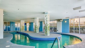 An indoor swimming pool with clear blue water, surrounded by blue walls and columns with green vines.