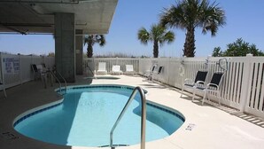 A swimming pool with a metal ladder, surrounded by white chairs and palm trees.