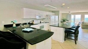 A modern kitchen with white cabinets, a black countertop, and a dining area with a long table and chairs.