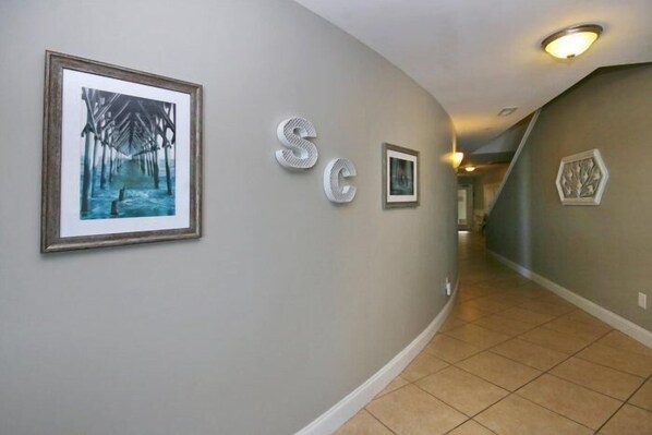 A hallway with a framed painting, decorative letters, and a hexagonal wall decoration.