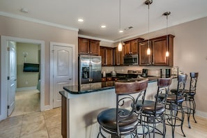 A modern kitchen with wooden cabinets, stainless steel appliances, and a bar area with stools.