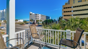 A balcony with chairs, a view of a building, and a street with palm trees. - South Beach Cottages - 2701 Apartment 4 (Myrtle Beach)