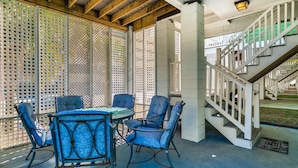 A covered outdoor seating area with a table and chairs, a staircase, and a view of a building in the background. - South Beach Cottages - 2701 Apartment 4 (Myrtle Beach)