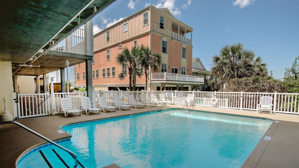 A swimming pool with lounge chairs and a building in the background. - Cherry Grove Villas - 204 Villa 6 (North Myrtle Beach)