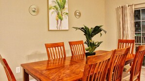 A dining area with a wooden table and chairs, a potted plant, and two wall-mounted decorative items. - Cherry Grove Villas - 204 Villa 6 (North Myrtle Beach)
