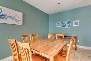 A dining room with a wooden table and chairs, teal walls, and artwork. - Cherry Grove Villas - 408 Villa 6 (North Myrtle Beach)