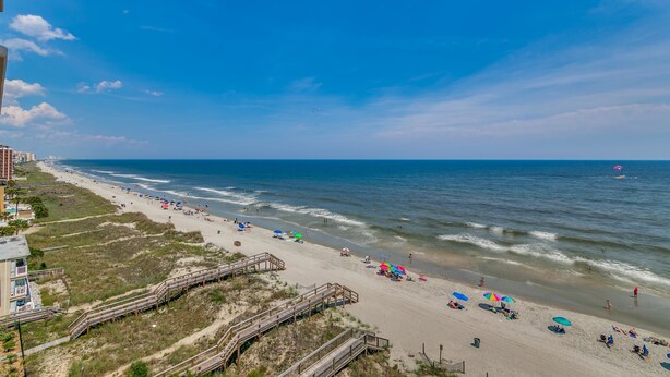 A beach with a wooden boardwalk, beach umbrellas, and people enjoying the shore.