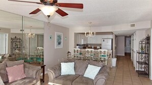 A living room with a ceiling fan, a dining area with a chandelier, and a kitchen with white cabinets. - Crescent Shores N - 703 Apartment 4 (North Myrtle Beach)