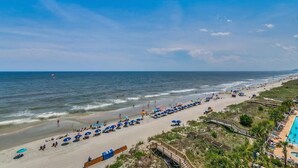 A beach with umbrellas and sun loungers, a swimming pool, and a boardwalk. - Crescent Shores N - 703 Apartment 4 (North Myrtle Beach)