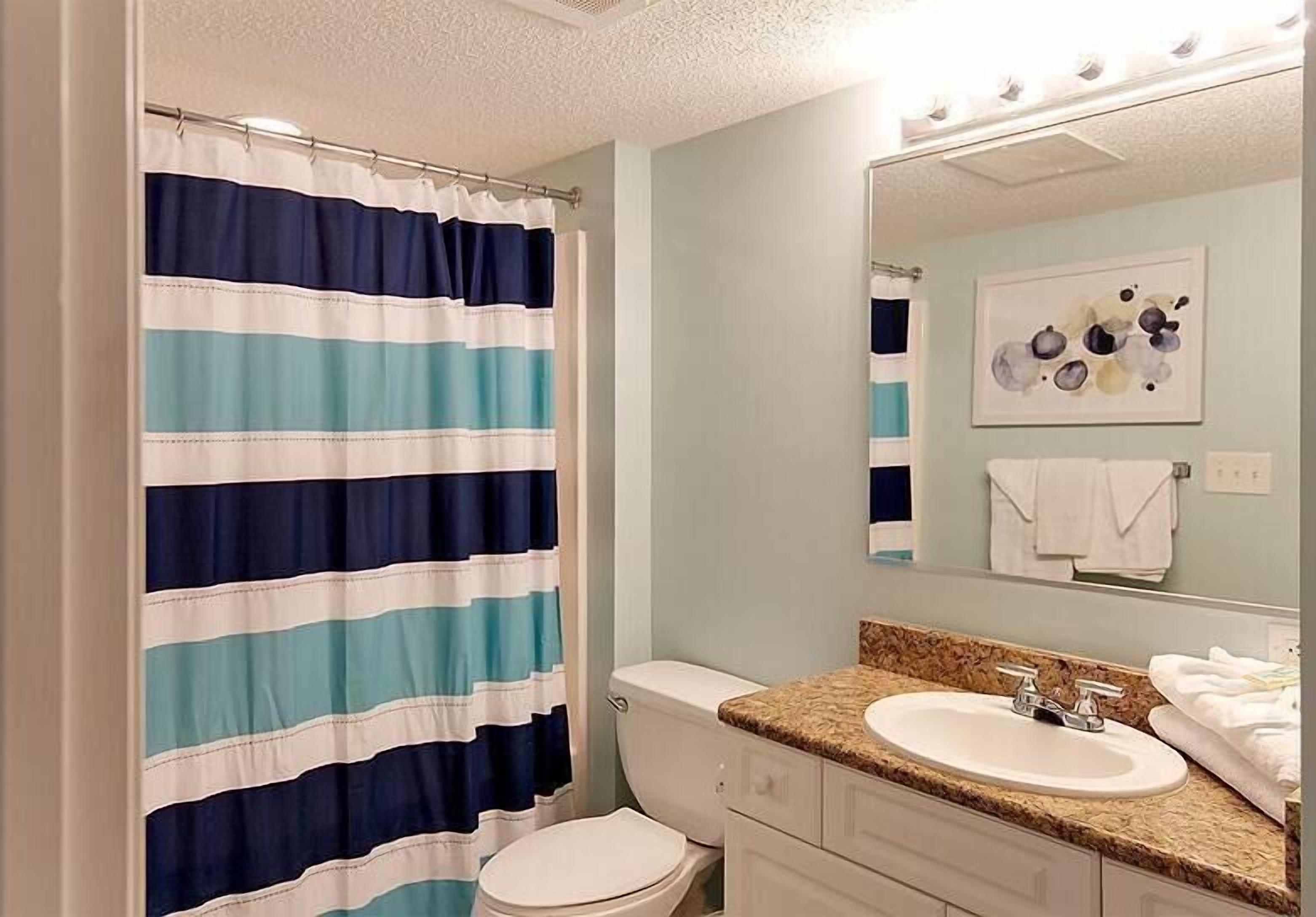 A bathroom with a striped shower curtain, a toilet, a sink with a mirror, and a towel rack.