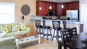 Una cocina moderna con armarios de madera oscura, un refrigerador de acero inoxidable y un microondas. Hay un comedor con una mesa y sillas de madera.