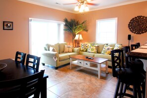 A living room with a sofa, coffee table, and chairs. There is a dining table with chairs, a lamp, and a plant. - South Beach Cottages - 2706 Apartment 4 (Myrtle Beach)