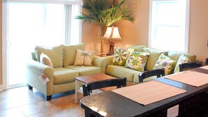 Una sala de estar con un sofá, una mesa de centro y una mesa de comedor con individuales. Hay una lámpara y una planta en la habitación.