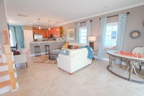 A spacious living area with a white sofa, a dining table, and a kitchen in the background.