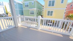 A wooden deck with a white railing, surrounded by colorful houses. - South Beach Cottages - 2716 Apartment 3 (Myrtle Beach)