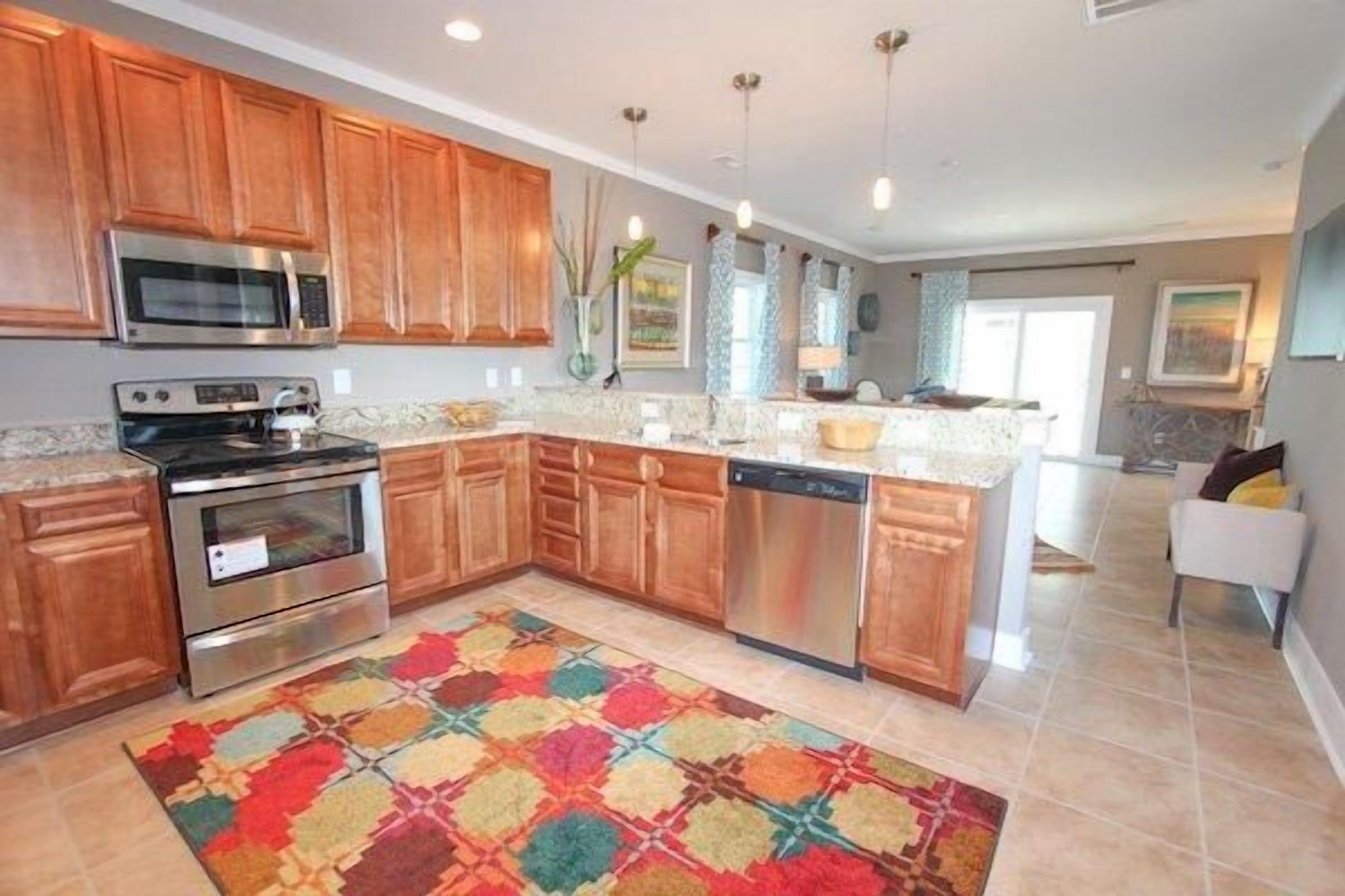 A kitchen with wooden cabinets, stainless steel appliances, and a colorful rug.