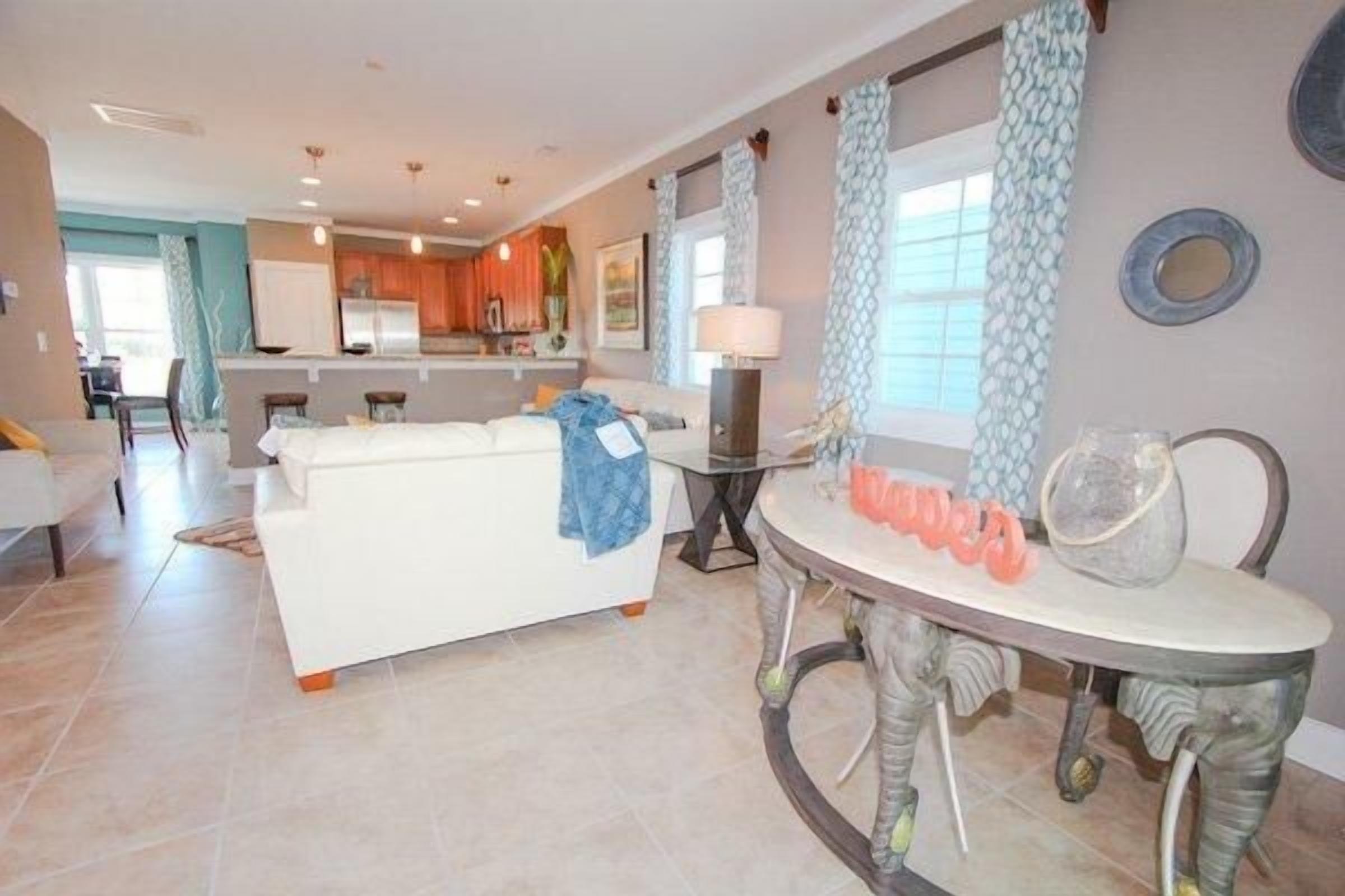 Una sala de estar moderna con un sofá blanco, una mesa de comedor con sillas y una cocina al fondo.